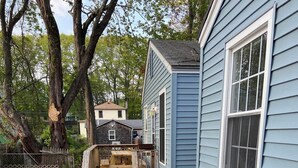 A wooden deck with picnic tables, a blue house, and trees in the background.