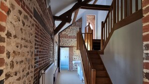 A narrow hallway with exposed brick walls and wooden beams, leading to a staircase with a wooden railing.