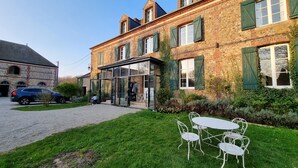 A traditional brick building with a glass entrance, a gravel driveway, and a grassy lawn with metal chairs.