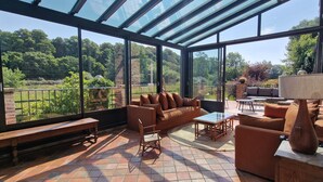 A sunlit patio with a glass-enclosed area, furnished with a sofa, chairs, and a table.