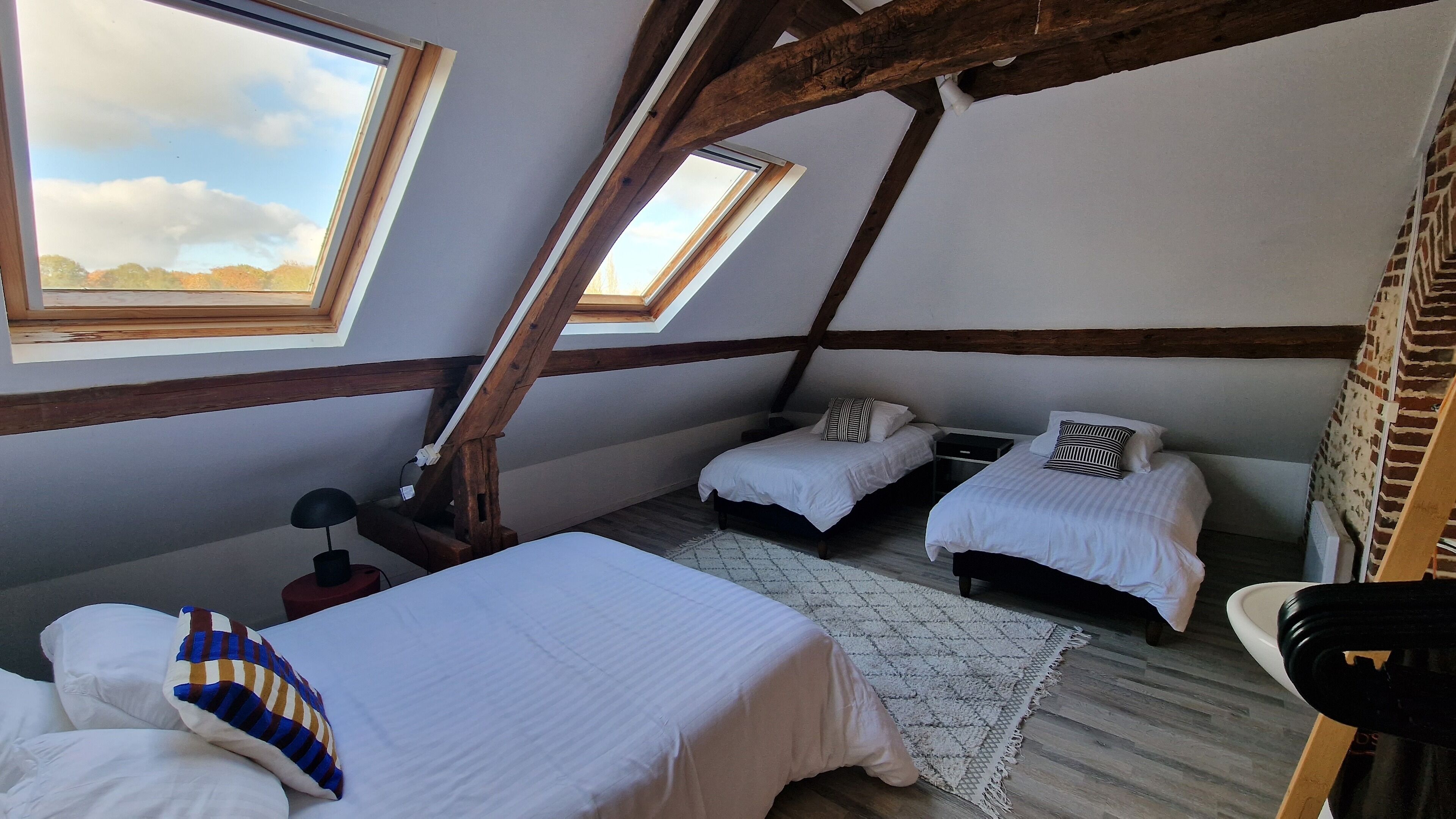 A room with two beds, a desk, and a chair. There are skylights and wooden beams.