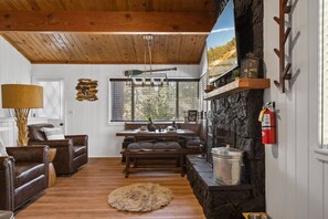 Una sala de estar acogedora con chimenea, techo de madera y comedor con una pared de acento de piedra.