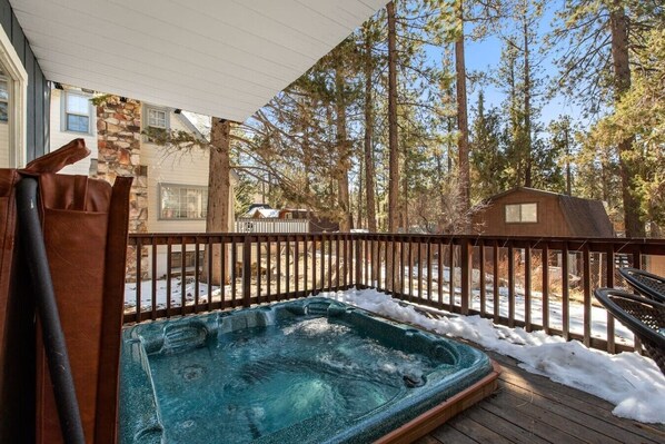 Un jacuzzi en una terraza de madera con un muro de piedra y un cobertizo de madera al fondo.
