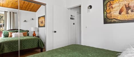 A hotel room with a green quilted bedspread, a wooden ceiling, a white door, and a wall-mounted sign.