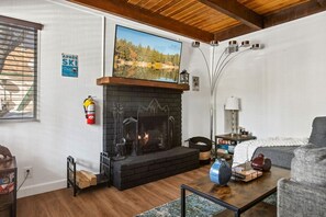 Una sala de estar acogedora con chimenea, un televisor montado encima y un rincón de estar confortable.