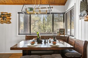 Comedor con mesa de madera, bancos y vistas amplias a través de grandes ventanales.