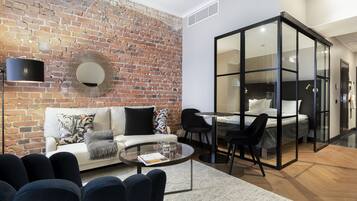 A modern living room with a brick wall, a sofa, a coffee table, and a glass-walled bedroom area.