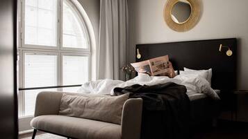 Un dormitorio con cama, un sillón de lectura, un espejo redondo y una ventana con persianas.