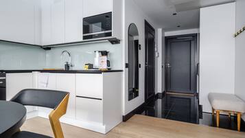 A modern kitchen with white cabinetry, a black countertop, a microwave, and a coffee maker.