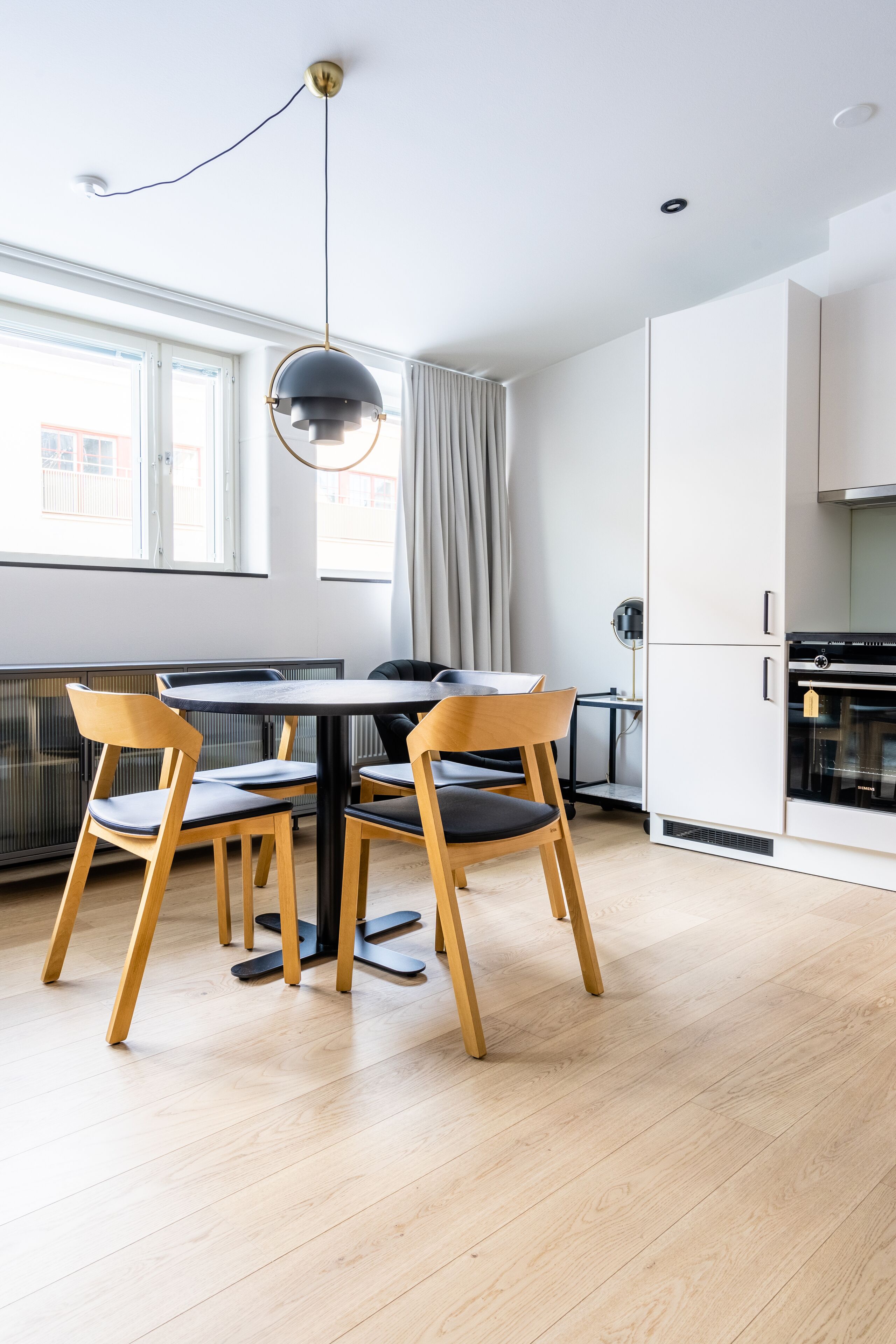 A modern kitchen with white cabinets, a black stove, and a dining area with a round table and wooden chairs.
