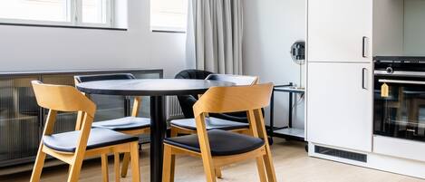 A modern kitchen with white cabinets, a black stove, and a dining area with a round table and wooden chairs.