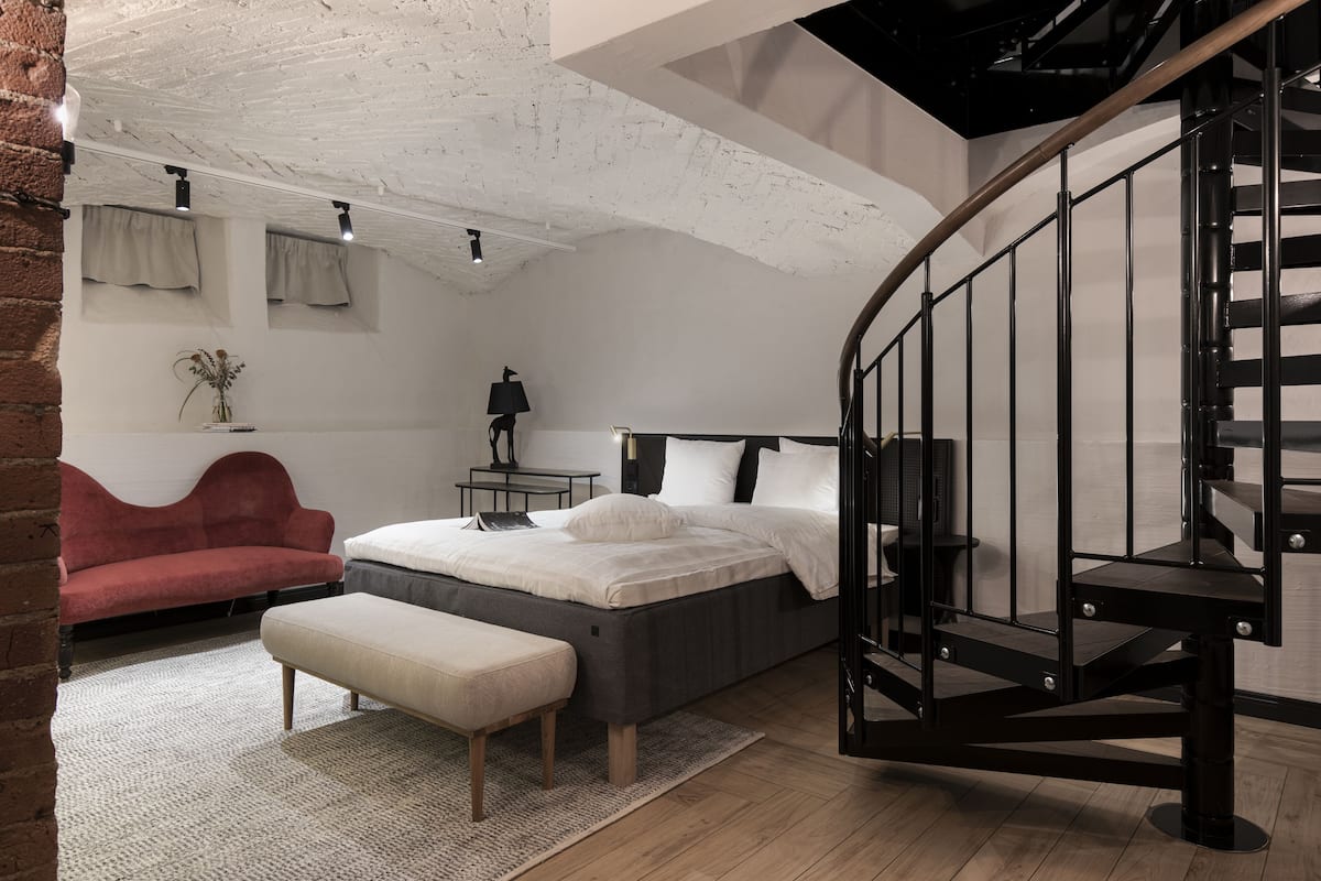 A modern bedroom with a curved staircase, a bed, a red sofa, and a small table with a lamp.
