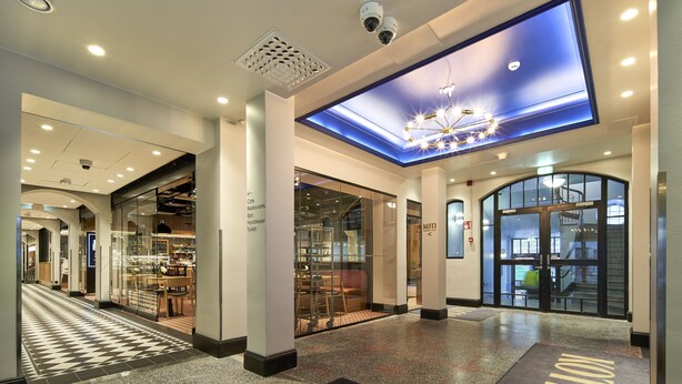 Eine Hotelhalle mit modernem Design, die einen zentralen, offenen Bereich, eine Glasfront und eine Decke mit eingelassener Beleuchtung und einem Oberlicht zeigt.