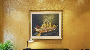 Una habitación con pared texturizada dorada, un cuadro enmarco de un barco, un mueble negro y un suelo con estampado.