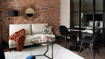 Una sala de estar moderna con pared de ladrillo, un espejo redondo, un sofá, una mesa de centro y un separador de vidrio que divide la sala de estar de un dormitorio.