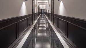 Ein langer, schmaler Korridor mit reflektierenden schwarz-weißen Fliesenböden, weißen Wänden und gleichmäßig verteilten Wandleuchten.