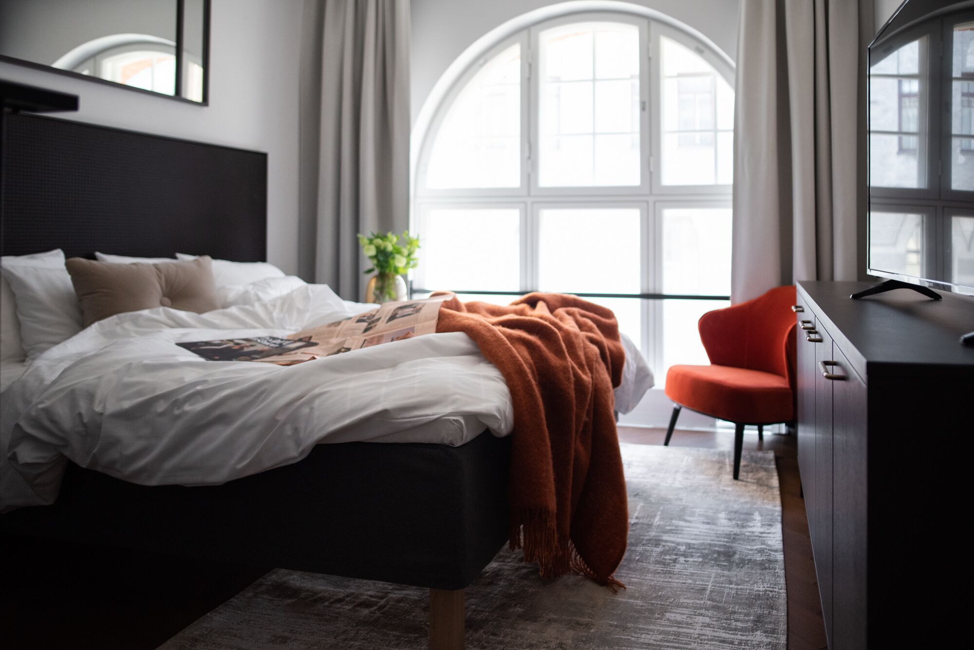 A modern bedroom with a bed, a desk, and a large window.