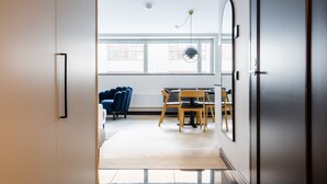 Ein offenes Durchgang zu einem modernen Wohnraum mit Essbereich, einer Couch und einem großen Fenster.