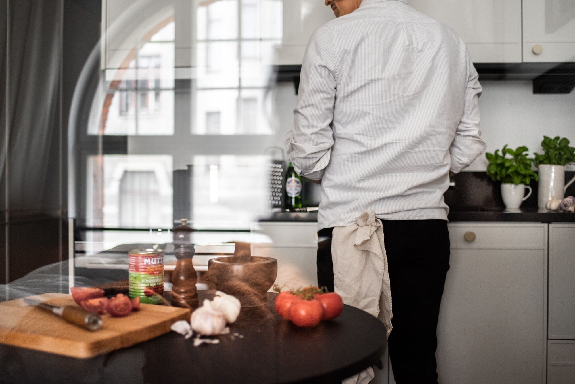 Una cocina moderna con una persona preparando comida, que incluye una tabla de cortar de madera, tomates frescos y una botella de aceite de oliva.