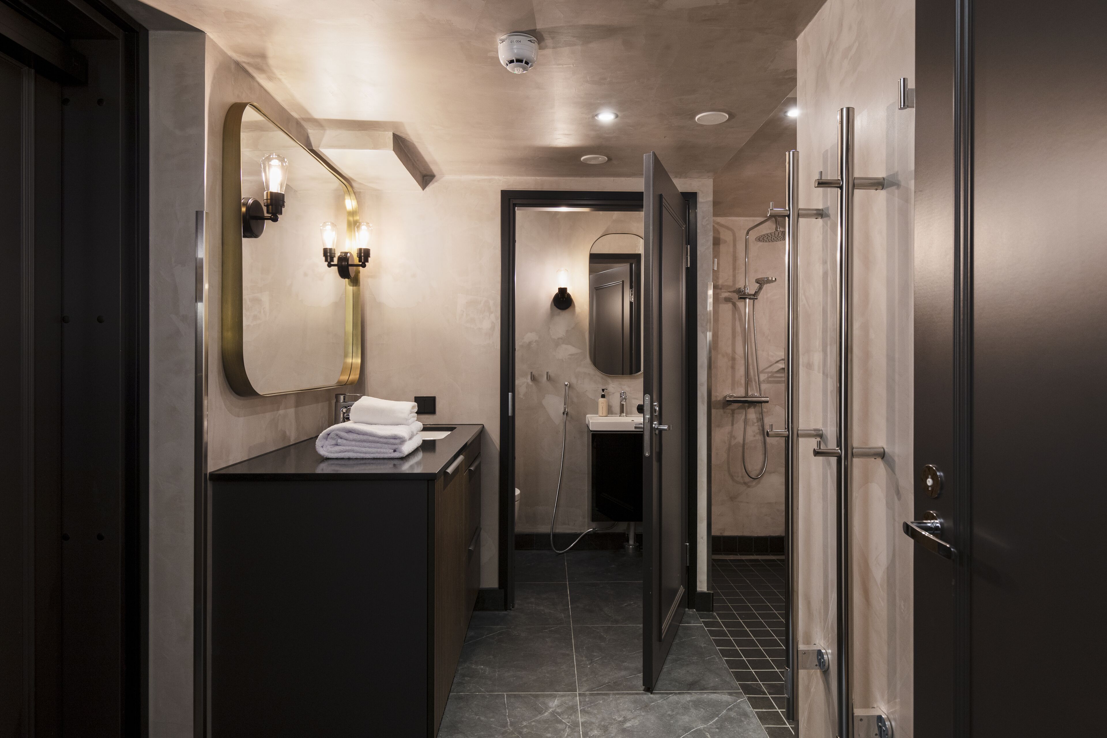 Un baño moderno con tocador oscuro, un espejo grande y una zona de ducha.