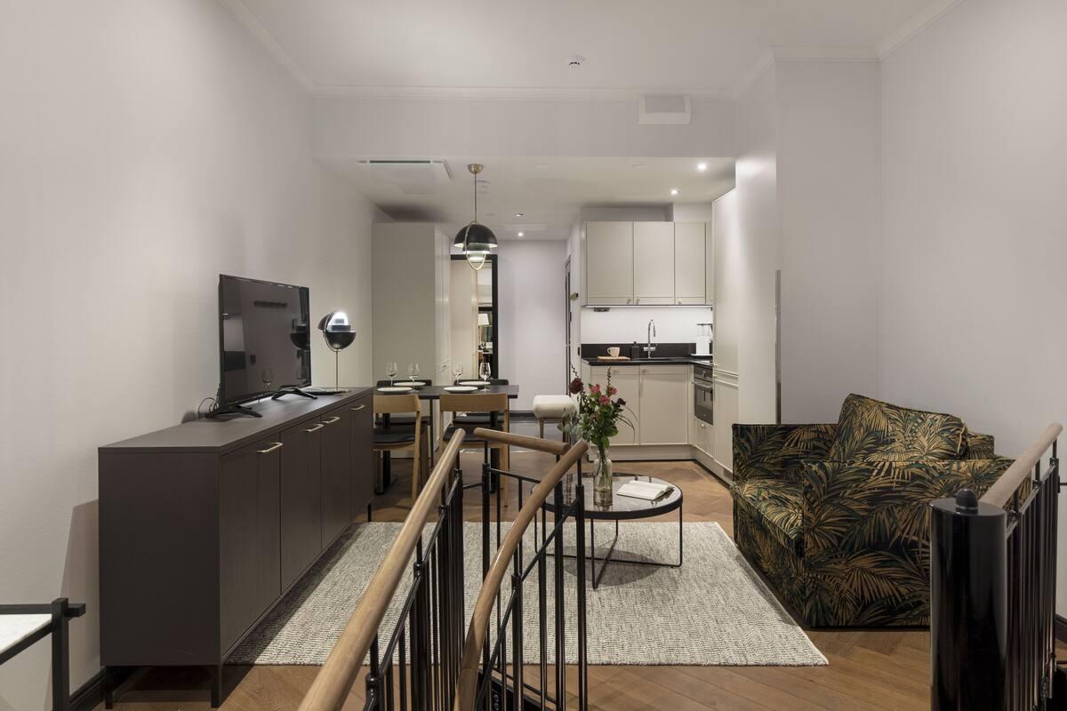 A modern living room with a sofa, a TV, a dining area, and a kitchen in the background.