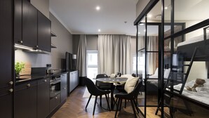 Eine moderne Küche mit dunklen Schränken, ein Essbereich mit rundem Tisch und Stühlen sowie ein Bett mit Blick.