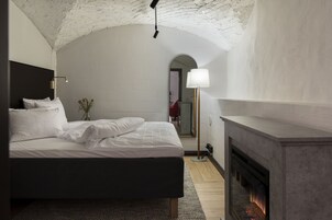 A bedroom with a bed, a fireplace, and a view of a hallway.