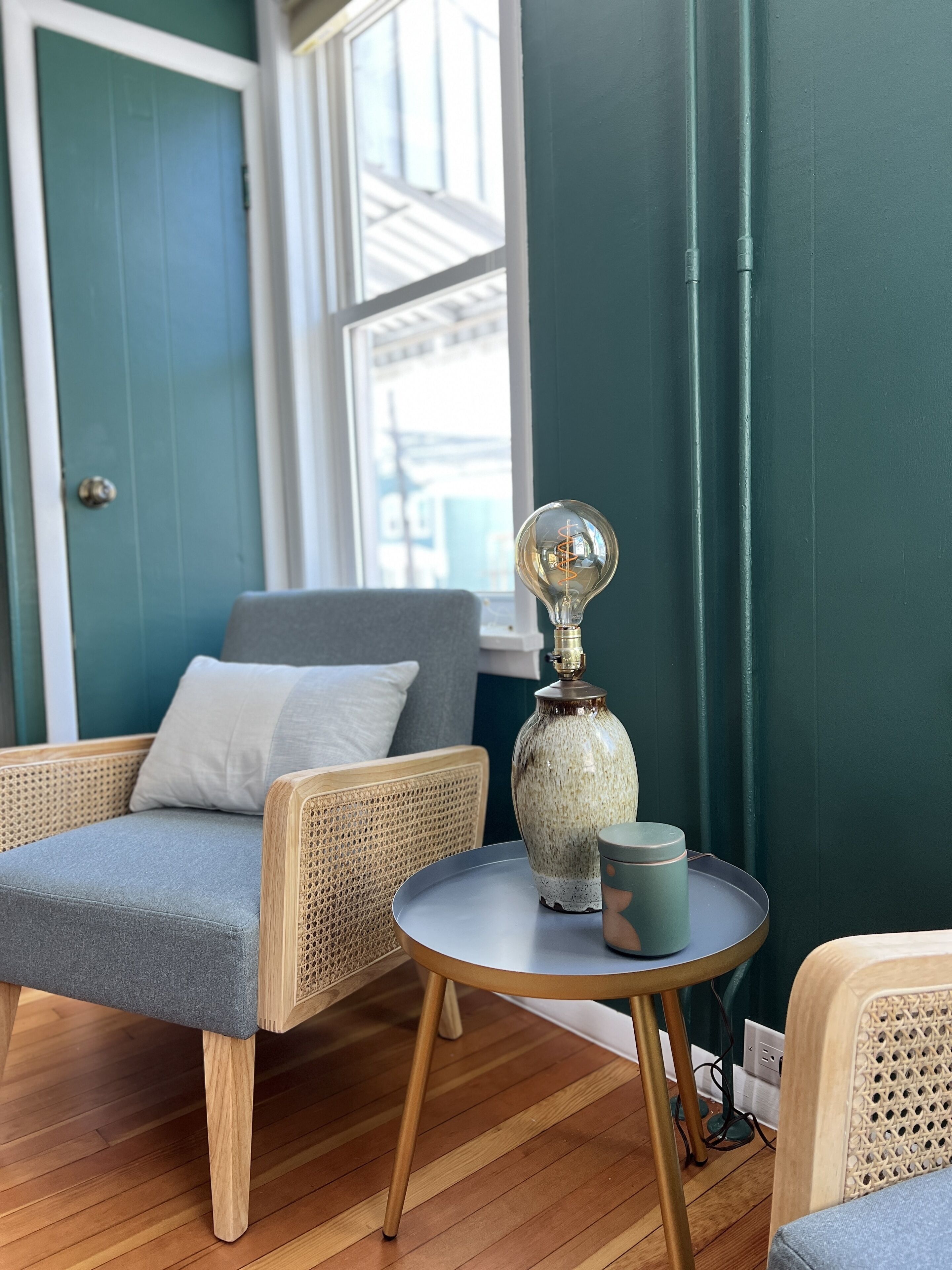 A cozy seating area with a wicker chair, a small round table, and a decorative lamp.
