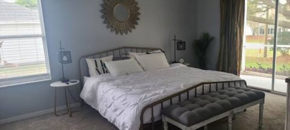 A bedroom with a large bed, a bedside table, a bench, and a window with a view of the outdoors.
