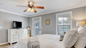 A bedroom with a bed, a TV on a dresser, a ceiling fan, and a window with blinds. - Spacious Condo, Walk to Beach, Heated Pool Access (Tybee Island)