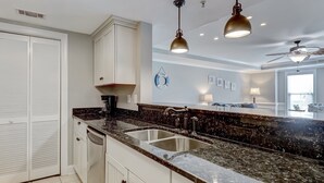 A modern kitchen with white cabinetry, a granite countertop, stainless steel sink, and pendant lighting. - Spacious Condo, Walk to Beach, Heated Pool Access (Tybee Island)
