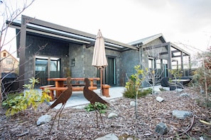 A modern building with a stone facade, a wooden bench, and a bird sculpture in the garden. - Black Stilt Retreat, STUNNING luxury property (Twizel)