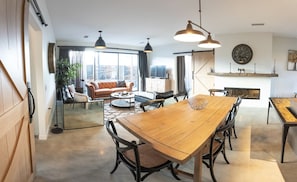 A modern living room with a wooden dining table, black chairs, a sofa, and a fireplace.