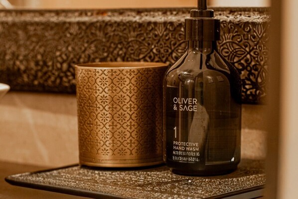 A bottle of Oliver & Sage protective hand wash and a patterned cup on a textured surface.