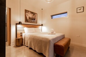 A bedroom with a bed, bedside lamp, a small window, and a framed picture on the wall.