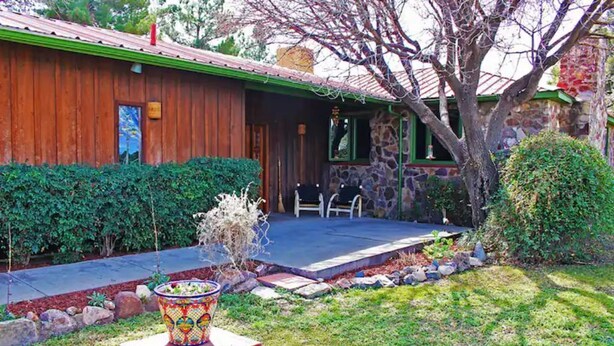 A wooden house with a covered porch, stone walls, and a small garden with a decorative planter. - Honey's Suite at The Sage Guesthouse formerly the 19th Hole (Alpine)