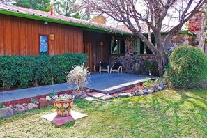 A wooden house with a covered porch, stone walls, and a small garden with a decorative planter.