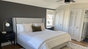 A bedroom with a large bed, a nightstand, a desk, a ceiling fan, and a patterned rug. - Modern Colonial House  (Yonkers)