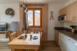 A dining area with a wooden table set for four, a television, and a view of buildings through a window. - 150m from resort center, 6th floor, view resort, swimming pool, sauna, terrace, balcony, ski locker (Les Orres)