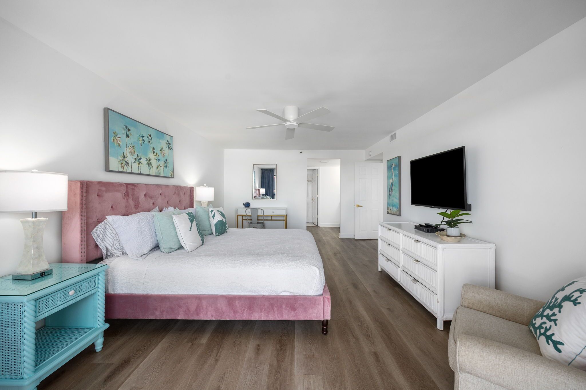 A bedroom with a bed, nightstand, dresser, TV, and artwork.