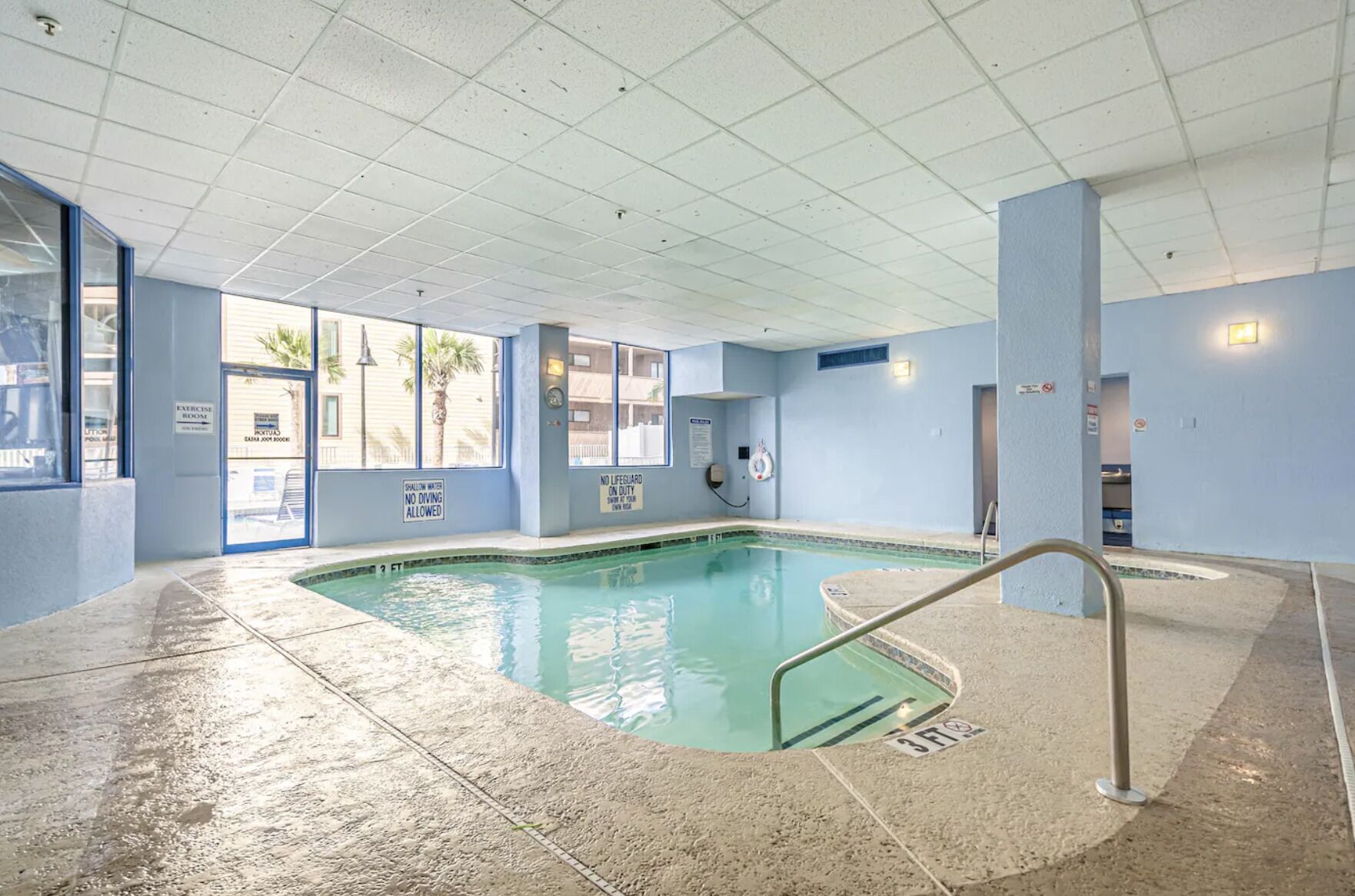 Piscina interior con señalización clara, incluyendo una zona prohibido bucear y una advertencia sobre aguas poco profundas.