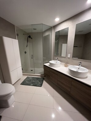 Un baño moderno con dos lavamanos, cabina de ducha de vidrio y un inodoro.