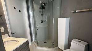 Un baño moderno con ducha envuelta en vidrio, inodoro blanco y tocador con lavamanos.