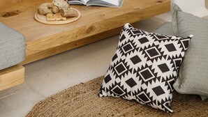 Un coin salon accueillant avec un banc en bois, un tapis tissé et un coussin à motifs.