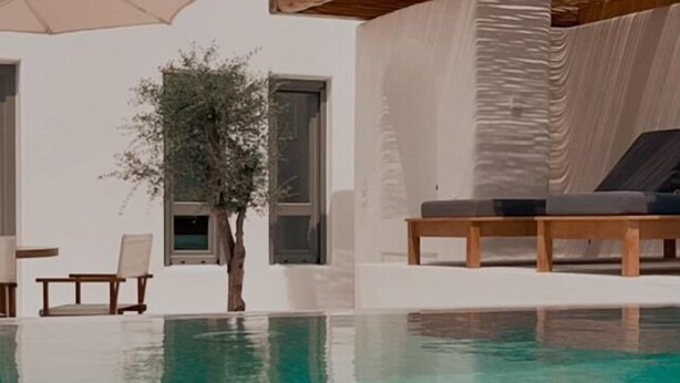 Un espace piscine moderne avec une eau cristalline, une terrasse en bois et un bâtiment blanc doté de grandes fenêtres.