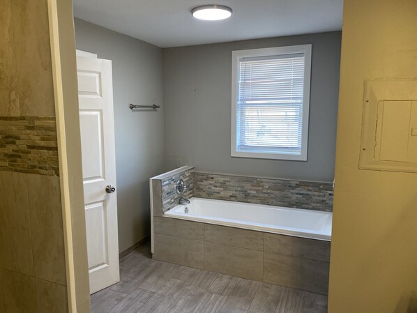 A bathroom with a bathtub, a window with blinds, and a door. - Guesthouse Farm Stay Near the Madison River! (Three Forks)