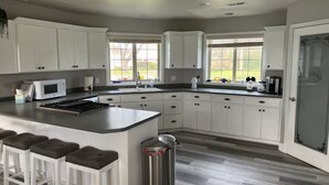 A modern kitchen with white cabinets, a central island with stools, a stainless steel trash can, and a window providing natural light. - Charming home on the Cliffs of Crescent City (Crescent City)