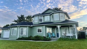 A two-story house with a green exterior, a front porch with a bench, and a garage. - Charming home on the Cliffs of Crescent City (Crescent City)