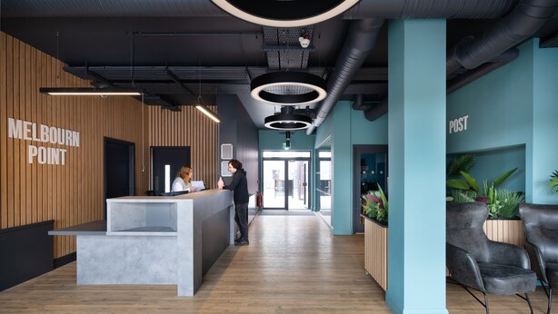 Una moderna area reception con parete rivestita in legno, una scrivania reception e un’area salotto con sedie nere.