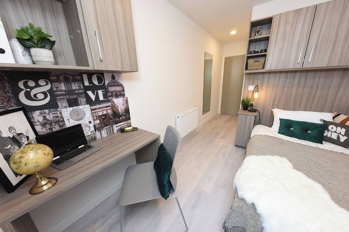 Ein modernes Schlafzimmer mit Schreibtisch, Laptop, Globus und einem Bett mit weißem Fellüberwurf.